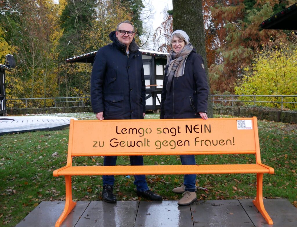 Bürgermeister Markus Baier und Gleichstellungsbeauftragte Christiane Osterhage (von links) vor der orangen Bank, die auf dem Kastanienwall den Blick auf das Thema der Gewalt gegen Frauen lenkt.